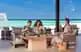 Beach club at resort in Maldives, with palm trees, white sand, and crystal-clear blue waters.